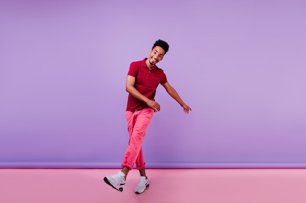Cara alegre e esportivo em calças cor de rosa, expressando felicidade. emocional jovem negro dançando.