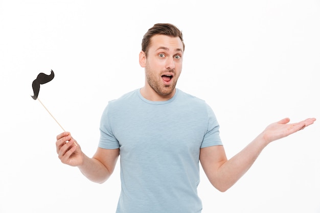 cara alegre em camiseta casual, segurando o bigode de papel na vara e gesticulando