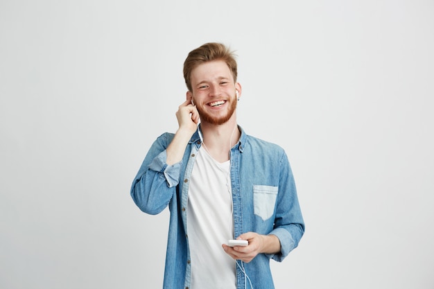 Cara alegre jovem em fones de ouvido, sorrindo, segurando o telefone ouvindo música.