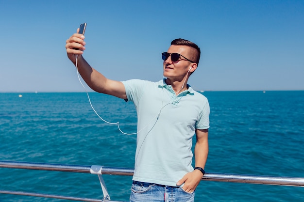 Cara alegre na moda em óculos de sol e fone de ouvido leva um selfie no telemóvel