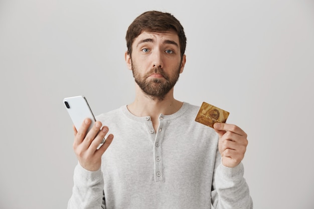 Cara barbudo chateado com cartão de crédito e smartphone