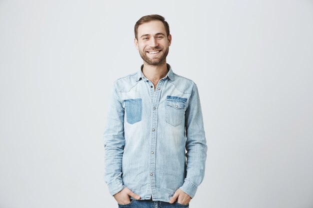 Cara barbudo sorridente amigável em pé na camisa jeans