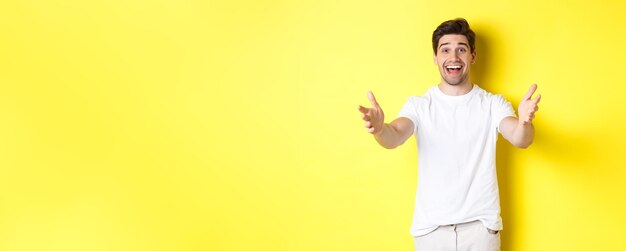 Cara bonito animado estendendo as mãos para a frente, alcançando o abraço, recebendo o presente em pé sobre o b amarelo