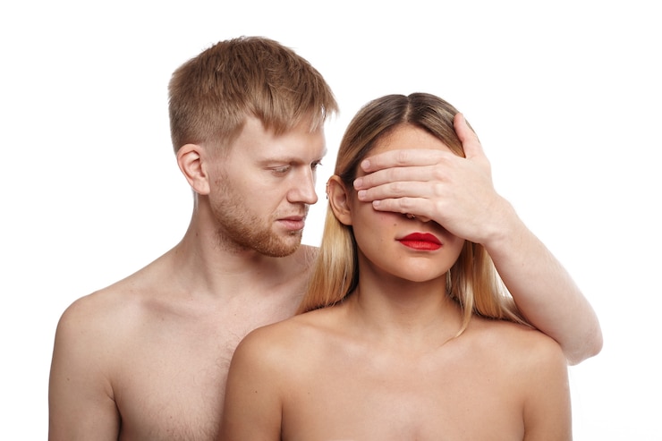 Foto grátis cara bonito com cabelo claro e barba por fazer em pé sem camisa atrás de uma atraente mulher nua e cobrindo os olhos com a palma da mão. pessoas, relacionamentos, intimidade, sentimentos, vida sexual e proximidade