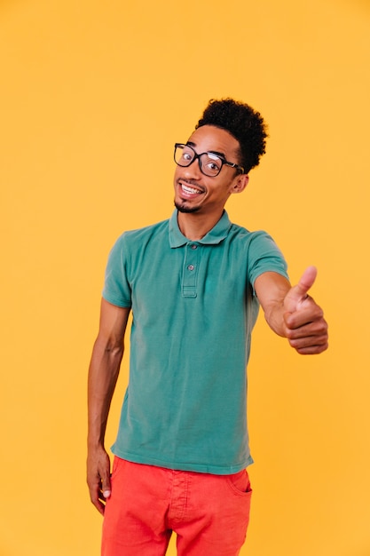 Cara bonito com expressão de rosto satisfeito em pé. Tiro interno do alegre homem moreno africano em copos grandes.