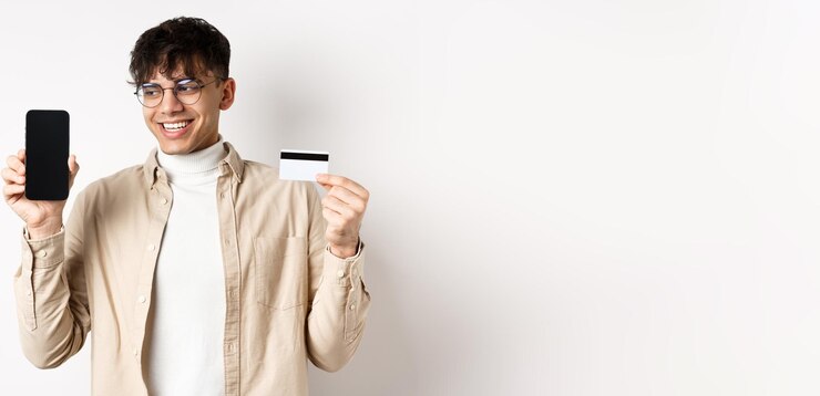 Foto grátis cara bonito de compras on-line em óculos mostrando tela de celular vazia e cartão de crédito sorrindo e l