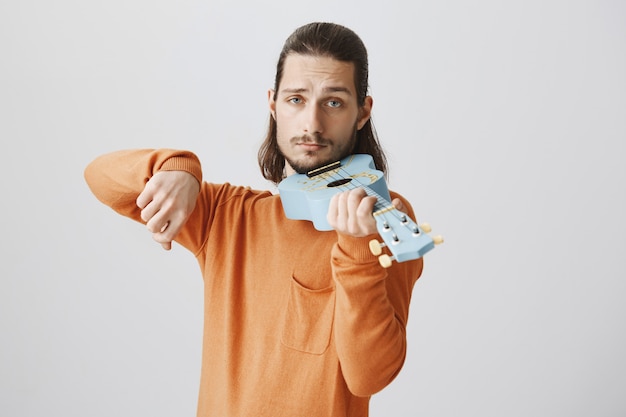 Cara bonito e engraçado segurando o ukulele como um violino