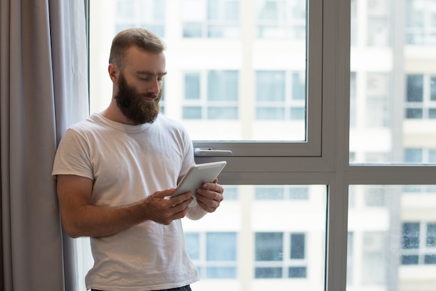 Cara bonito hipster sério usando tablet digital em casa