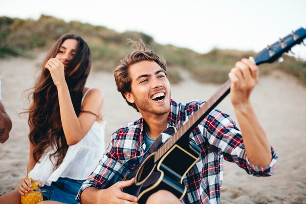 Cara com guitarra cantando na praia