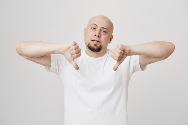Cara de barba careca cético mostrando o polegar para baixo e decepcionado