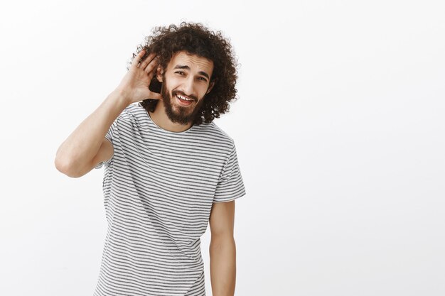 cara despreocupado e bonito com barba e penteado afro, segurando a mão perto da orelha e fazendo perguntas