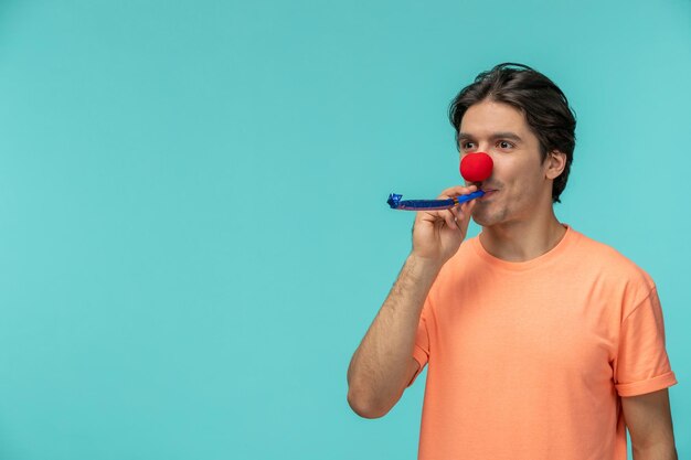 Cara do dia da mentira segurando um apito palhaço de nariz vermelho engraçado camiseta laranja morena