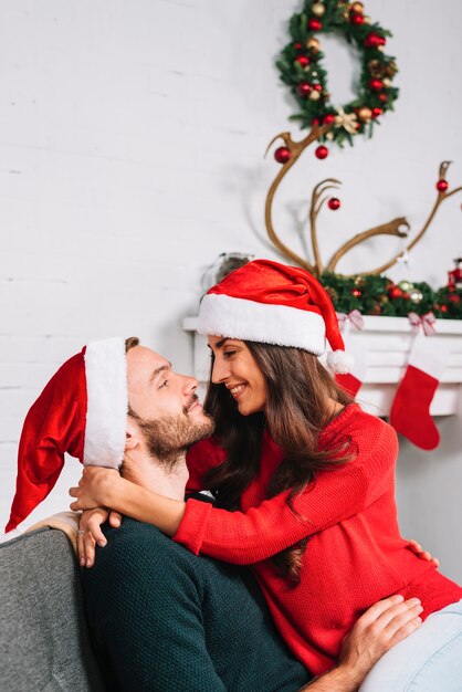 Cara e mulher em chapéus de Natal abraçando no sofá