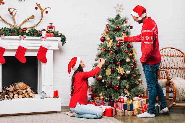 Cara e mulher vestindo árvore de Natal com enfeites