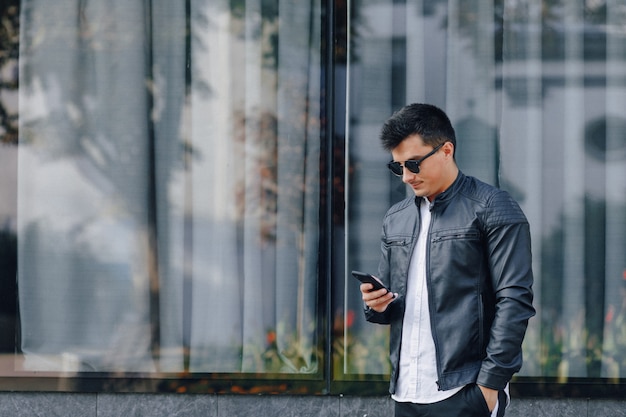 Cara elegante jovem de óculos na jaqueta de couro preta com telefone