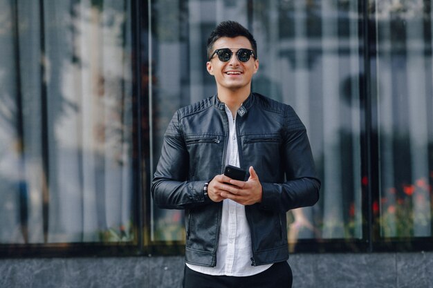 Cara elegante jovem de óculos na jaqueta de couro preta com telefone