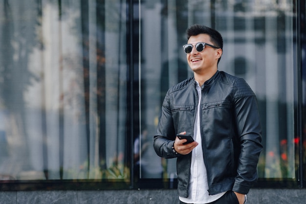 Cara elegante jovem de óculos na jaqueta de couro preta com telefone