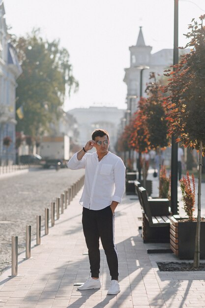 Cara elegante jovem em uma camisa andando por uma rua europeia em um dia ensolarado