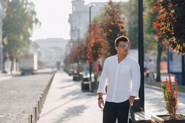 Cara elegante jovem em uma camisa andando por uma rua europeia em um dia ensolarado