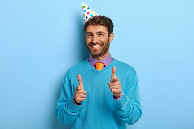 Cara encantado com chapéu de aniversário posando de suéter azul