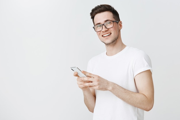 Cara feliz e sorridente de óculos usando telefone celular e olhando