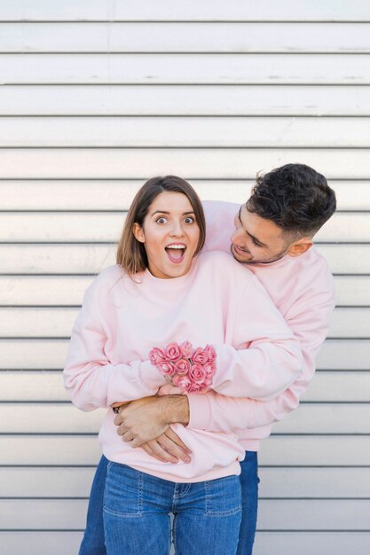 Cara jovem abraçando atraente espantada senhora com flores