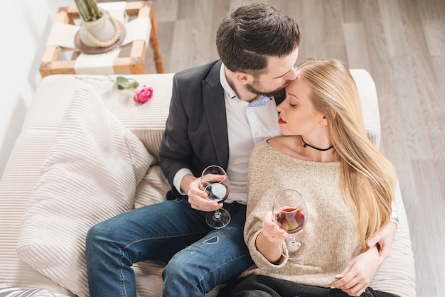 Foto grátis cara jovem beijando na frente da senhora com taças de vinho e sentado no sofá na sala