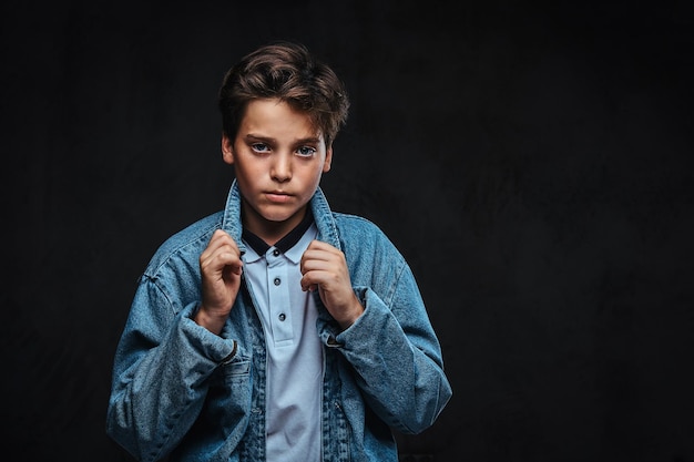 Cara jovem elegante vestido com uma camiseta e jaqueta jeans posando em um estúdio. Isolado no fundo escuro.