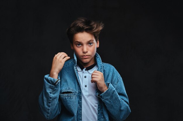 Cara jovem elegante vestido com uma camiseta e jaqueta jeans posando em um estúdio. Isolado no fundo escuro.