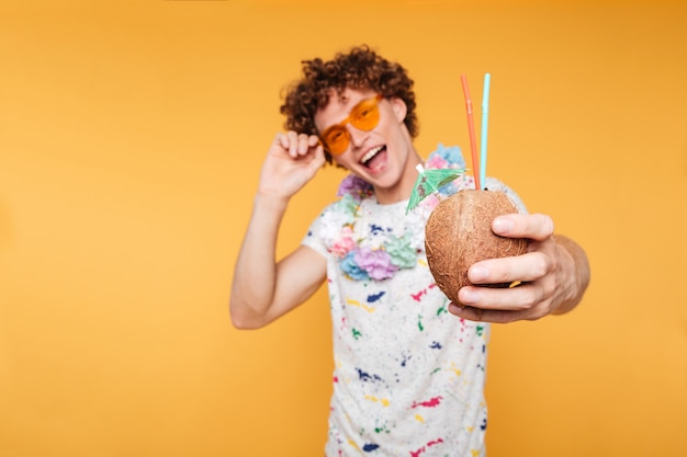 Foto grátis cara jovem feliz em óculos de sol mostrando coquetel de coco