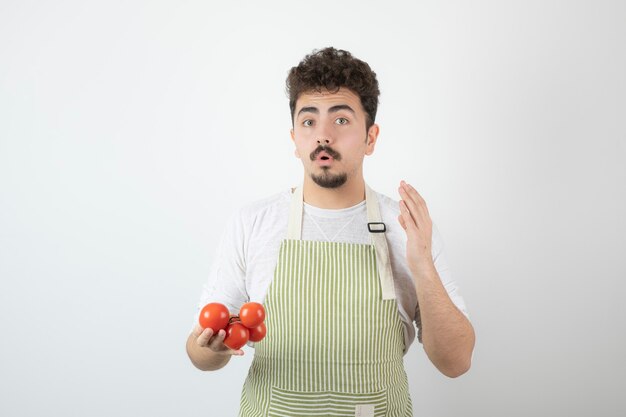 Cara jovem pensativo segurando a pilha de tomates e levantando a mão.