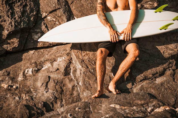 Cara jovem, segurando a prancha de surf perto de pedras