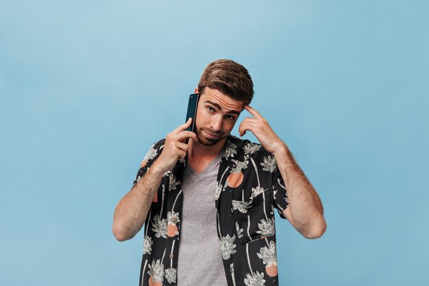 Cara legal barbudo em elegante camisa de manga curta preta e camiseta olhando para a câmera e falando no telefone em fundo isolado