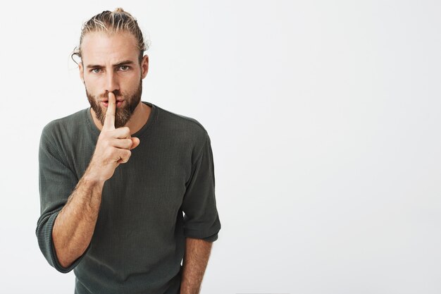 Cara madura bonita com penteado elegante e barba segurando o dedo indicador nos lábios, pedindo silêncio