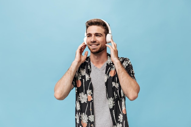 Cara maravilhoso com penteado legal em camisa de manga curta preta pintada e camiseta cinza olhando para longe e ouvindo música