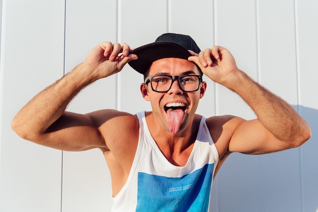 Cara muscular alegre em óculos e boné mostrando uma língua na câmera