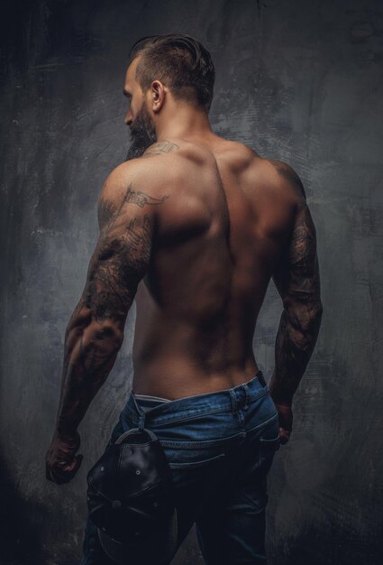 Cara musculoso sem camisa de volta em jeans azul com mãos tatuadas.