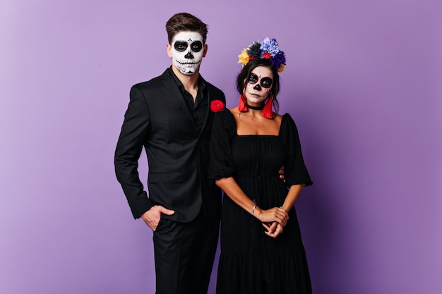 Cara sério, com o rosto pintado e menina com flores no cabelo, posando para um retrato para o halloween.