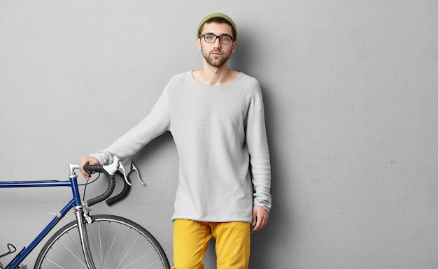 Cara sério vestido casualmente, vendendo bicicletas modernas, mantendo as mãos no guidão, demonstrando sua boa qualidade para os clientes. Jovem sportrsman indo em outra cidade de bicicleta. Conceito de equitação