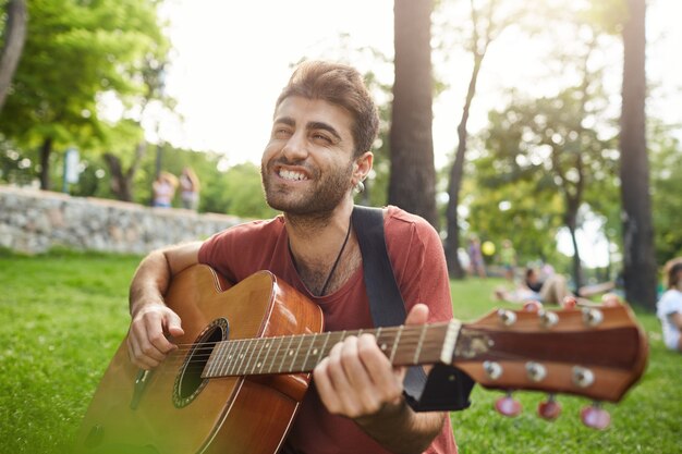 Cara sorridente e despreocupado cantando música e tocando violão no parque