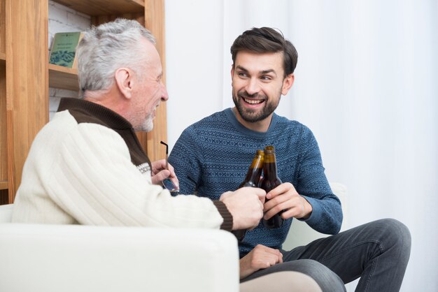 Foto grátis cara sorridente jovem clanging garrafas com homem envelhecido no sofá