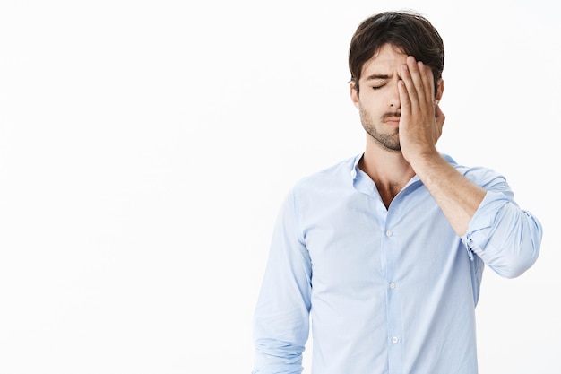 Cara triste, perdendo a oportunidade de sua vida sendo culpado e chateado, fazendo gesto com a palma da mão no rosto com a mão no rosto em pé com os olhos fechados, sentindo-se exausto e inquieto após o fracasso sendo demitido