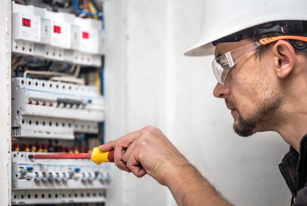 Cara, um eletricista trabalhando em uma central telefônica com fusíveis. instalação e conexão de equipamentos elétricos. fechar-se.