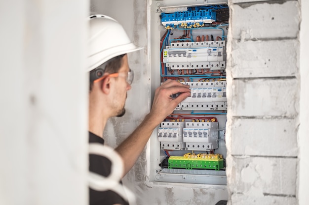 Foto grátis cara, um eletricista trabalhando em uma central telefônica com fusíveis. instalação e conexão de equipamentos elétricos.