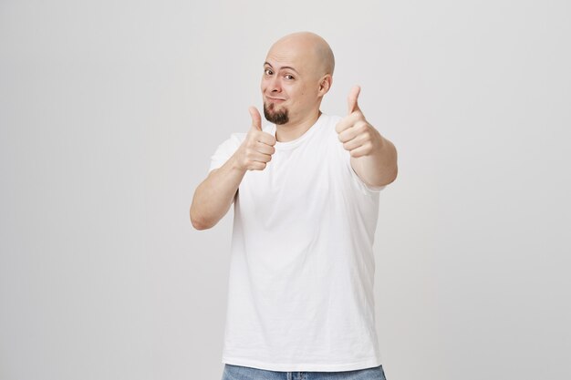 Careca bonito sorrindo, mostrando o polegar para cima em aprovação