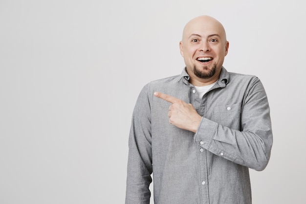 Careca feliz empolgado apontando o dedo para a esquerda, sorrindo