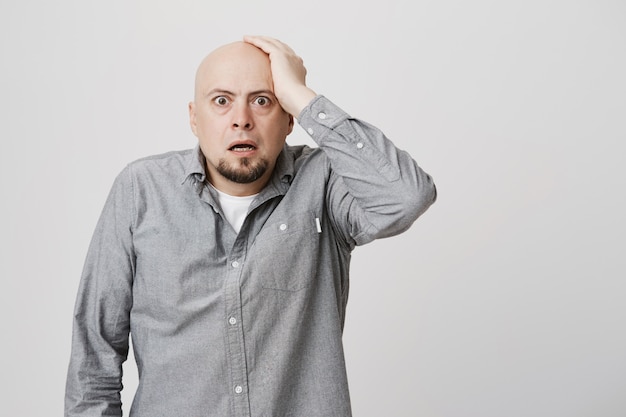 Foto grátis careca perplexa e preocupada, segurando a mão na cabeça e olhando confusa