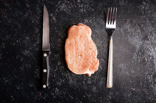 Carne de bife cru na mesa de madeira preta ao lado de garfo e faca. Comida gourmet e refeição crua fresca