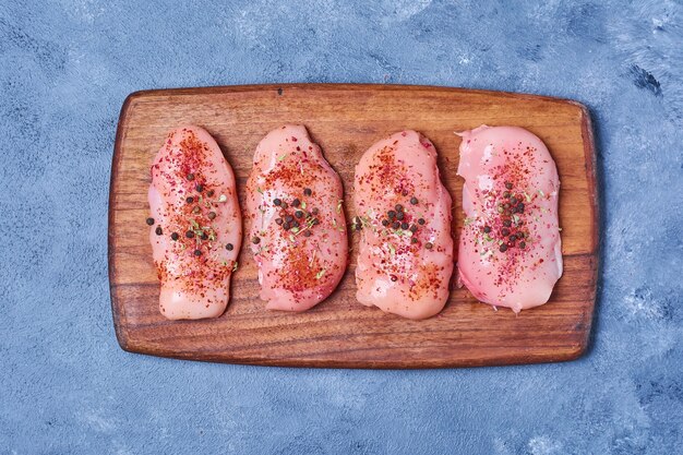 Carne de frango com especiarias em uma placa de madeira em azul