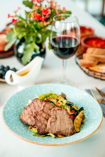 Carne frita com berinjela e tomate, servida com um copo de vinho